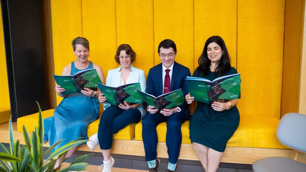 GBA team members pose reading a report published by the organization in front of a yellow wall