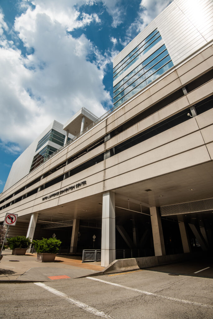 Facade of a modern multi-story building with large glass windows and a parking garage. The structure is set against a blue sky with few clouds.