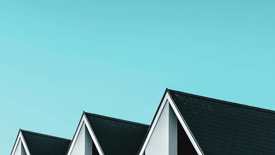 The rooftops of several houses with black slanted roofs against a clear light blue sky.