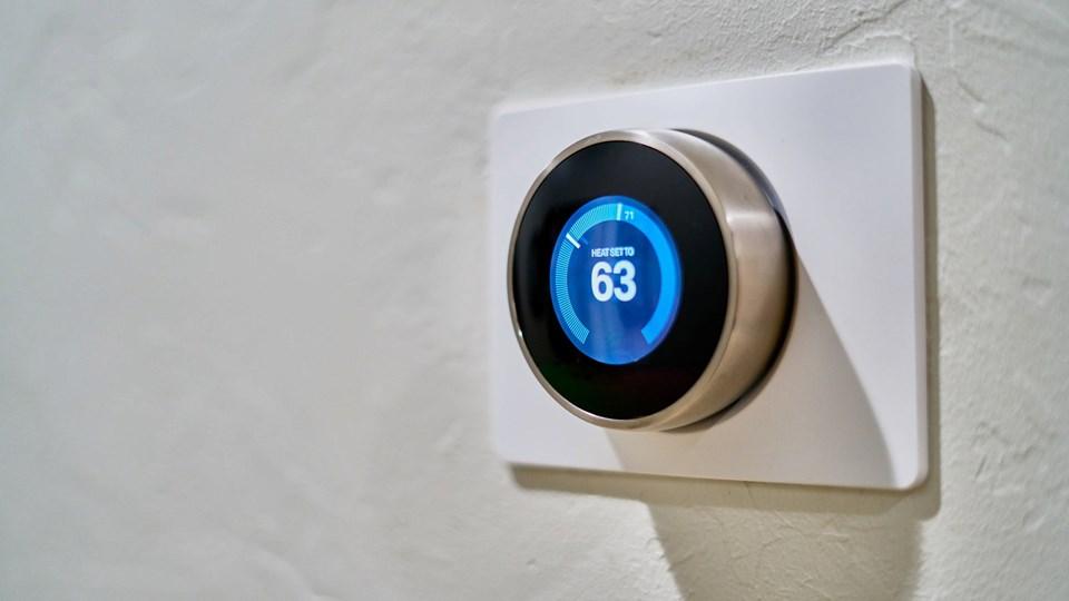 A round digital thermostat mounted on a white wall shows a blue display with the temperature set at 63 degrees.