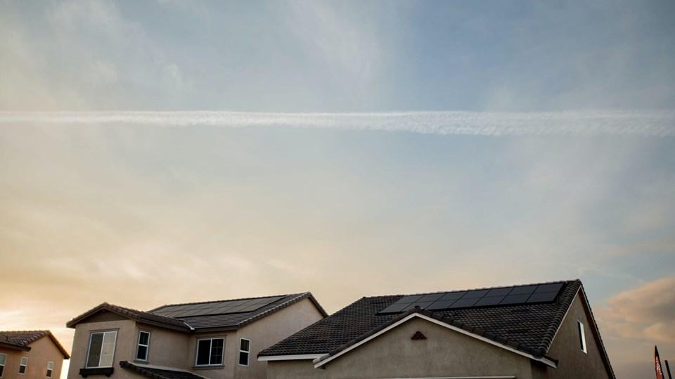 Two residential houses with solar panels on their roofs under a cloudy sky.