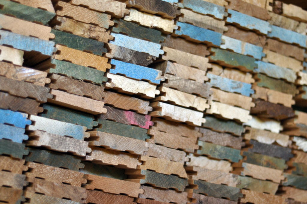 Stacked wood samples in various shades and finishes including blue, brown, and cream, arranged in a pattern. Each piece is cut with interlocking edges.